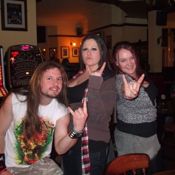 A young man with a beard and long hair and 2 young girls posing and giving the sign of the horns.